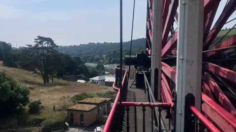 The new modern looking sshed with a turf roof- sits in the background next to the enormous red Laxey wheel.