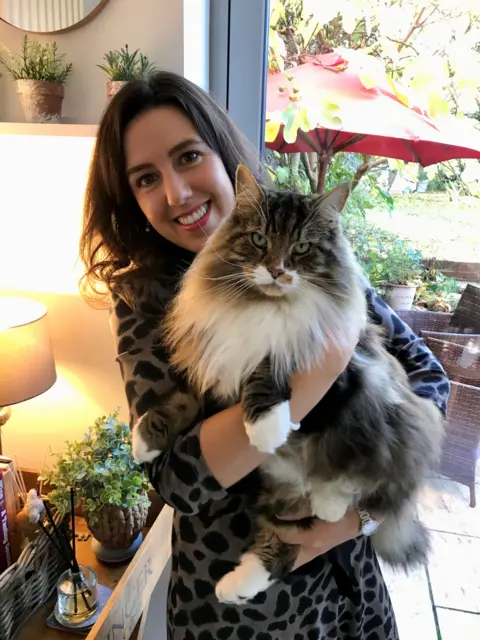 Laura Ancell Woman holding large cat with big white mane