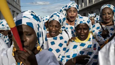 AFP Women dressed in a patterned white a blue outfit with horn blowers. They are celebrating