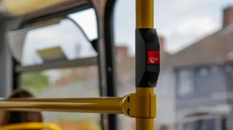 A generic image from inside a bus of a stop button. Houses are blurred in the background.
