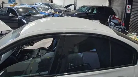 Several high-end cars, including BMWs, Mustangs and Range Rovers in various states of disrepair in a garage