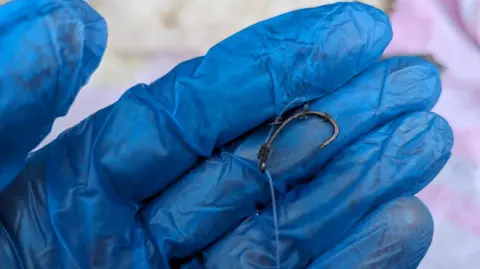 Fish hook and line in a gloved hand