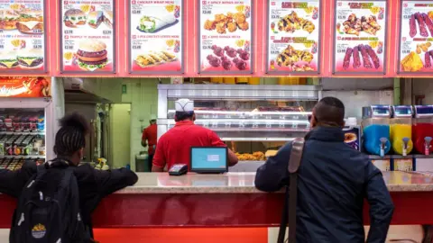 Jack Taylor/Getty Images Customers wait to be served at a fast food takeaway