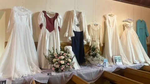 A range of dresses hanging from the wall in various colours, one of them light blue. 