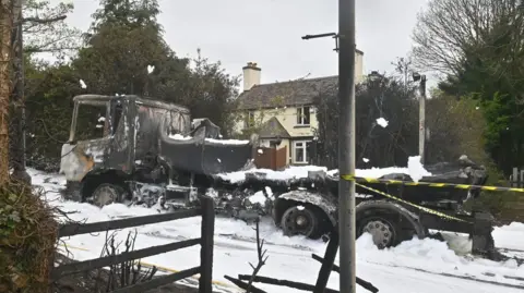 Shropshire Fire and Rescue Service The blackened shell of a lorry in a street covered in white foam, with a cream coloured house in the background and a lamp post and fence in the foreground