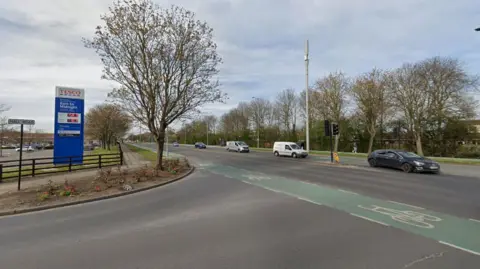 Google Cars travelling down a two-lane road. On the left is a Tesco petrol board showing and next to it is a road sing reading "Hall Road".