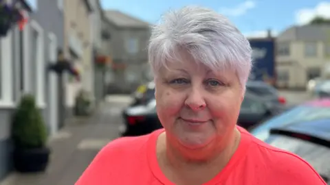 Donna Nugent in Ederney.  She smiling at the camera with short, grey hair and she is wearing a bright pink top