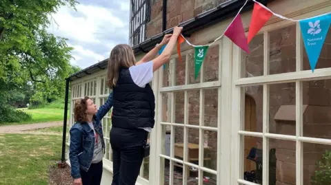 Two women putting up National Trust bunting on the outside of a house