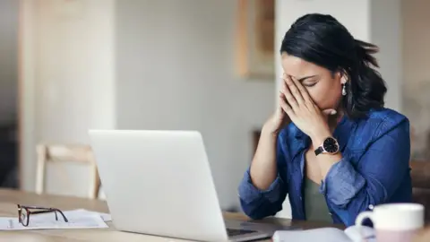 Getty Images Woman behind computer with head in her hands