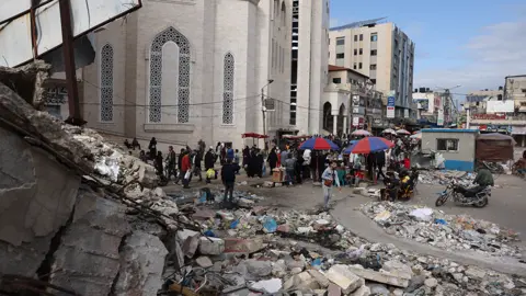 Getty Images People walk pass market stalls and destroyed buildings in Khan Younis