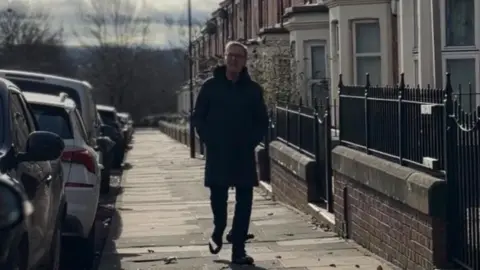 BBC Alan Milburn on a street in Newcastle. He is wearing a dark coat and has his hands in the pockets.