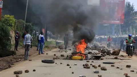 Anadolu via Getty Images People stand next to a burning tyre on a road littered with stones