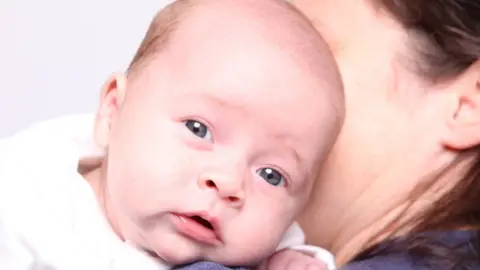 BBC Baby being held by his mother, part of a couple from Ireland who travelled to Ukraine for surrogacy