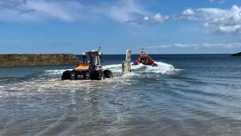 Pete Collinson/Cullercoats RNLI Launch Authority A lifeboat launches out to sea at Cullercoats Bay. A tractor has driven out into the water to help launch the vessel.