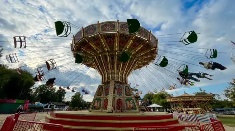 BBC Weather Watcher, Annabel Henley on Thames, Oxfordshire - chair swing fairground ride with the swings stretched out as it goes round.