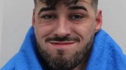 Met Police A close-up portrait of a man with short dark hair and a trimmed beard, wearing a blue garment and looking at the camera with a slight smile.