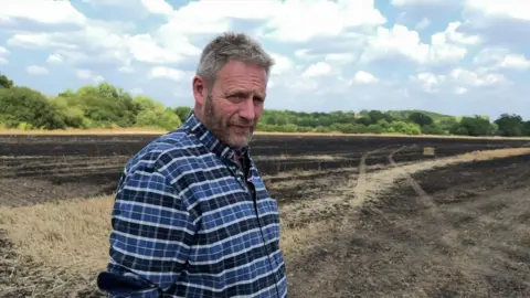 A farmer stands on a field that is charred and scorched from a fire. 
