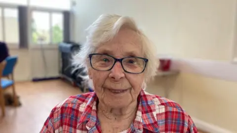 Kay Drinkwater with glasses, grey hair and red shirt