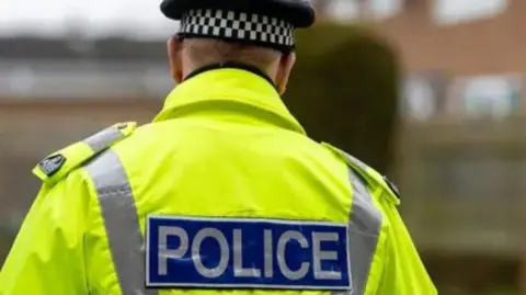 Police officer standing with his back to the camera wearing a hat.