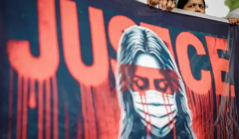 Banner with the word justice written in red, with red lines dripping from the base of the letters, like blood; an image of a woman wearing a surgical mask is also depicted