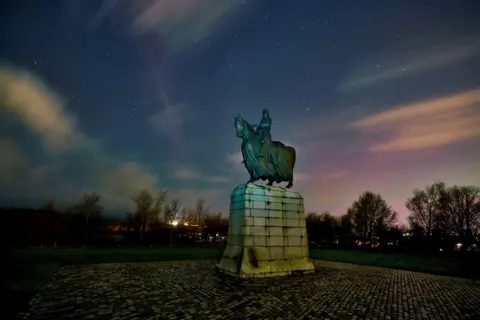John Cuthbert Monument of King Robert the Bruce, tinged green with age, on a plinth below a vivid sky of blue and pink.