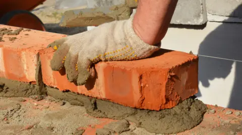 Builder's hand lays a brick in mortar on a wall