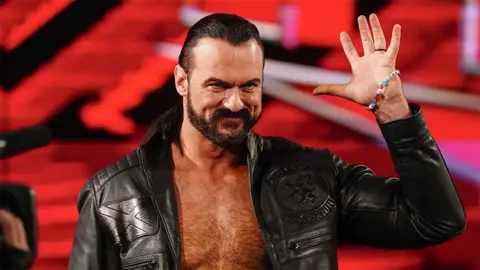 Getty Images A male wrestler wearing a black leather jacket with his left hand raised