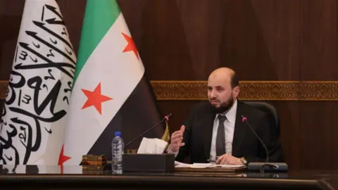 Telegram Mohammed al-Bashir, the prime minister of Syria's new transitional government, speaks at a meeting with ministers in Damascus (10 December 2024)