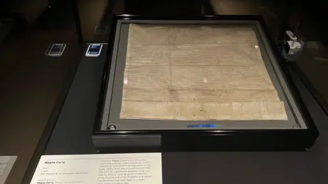 The charter is in a glass box in a frame with low lighting and a description sits by its side at the front.