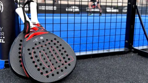 Padel raquets next to a padel court with blue flooring.