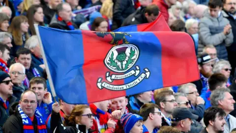 SNS An Inverness Caledonian Thistle flag is held aloft above a crowd of fans.