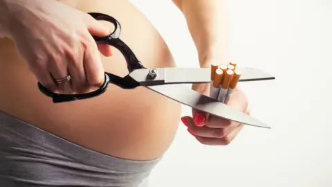 grinvalds/Getty pregnant woman cutting up some cigarettes