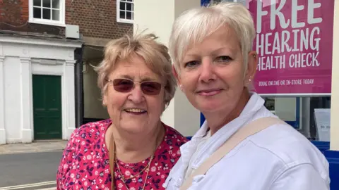 Two ladies taking to the BBC in Blandford. One is wearing a red floral top, the other, a white jacket.