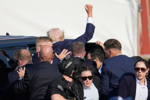 AP Republican presidential candidate former President Donald Trump is helped off the stage at a campaign event in Butler, Pa., on Saturday, July 13, 2024.