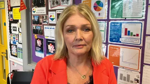 BBC Bernie Davis has shoulder length blonde hair and blue eyes, and is wearing a red blazer as she stares at the camera.