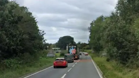 A section of the A66 at Kirkby Thore. The road is single carriage with several vehicles and a 40mph sign can be seen in the distance. There are fields and trees either side of the road. 