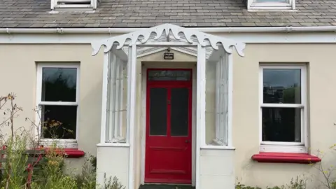 A house with a red door and a sign above it saying 'Vazon Cottage'