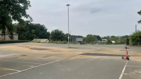 Tom Percival/BBC A dusty car park with a red scooter off to the right hand side. 