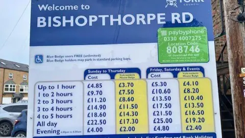 A parking board showing prices at Bishopthorpe Road car park. Up to one hour costs £4.85 and all day parking costs £22.50 from Sunday to Thursday.