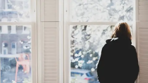 Getty Images Woman standing by a window looking out