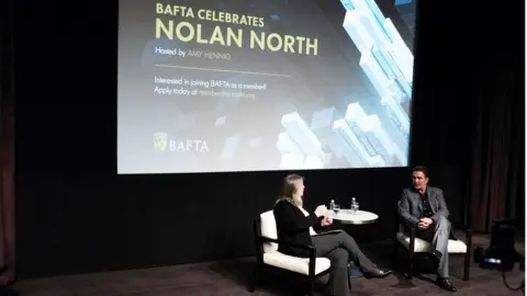 Getty Images Amy Hennig interviews Nolan North on stage before he accepts his BAFTA