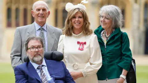 PA Media Kate Garraway, with her husband Derek Draper and her parents Gordon and Marilyn Garraway, after being made a Member of the Order of the British Empire for her services to broadcasting, journalism and charity by the Prince of Wales during an investiture ceremony at Windsor Castle, Berkshire