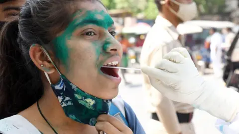 EPA A health worker takes a swab sample to test for COVID-19 in Delhi, India, 26 March 2021.