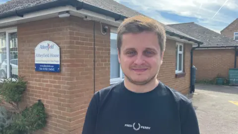 A head and shoulders picture of Castle Point councillor, Tom Gibson, with Abbeyfield House behind him