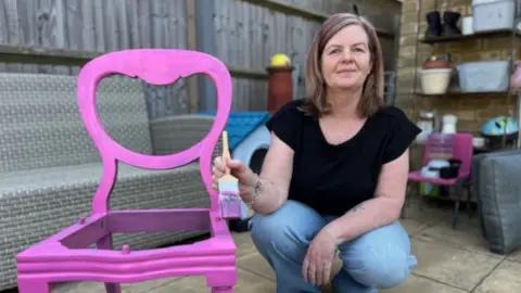 Paula Desai, a furniture restorer and novelty card maker, paints a pink chair.
