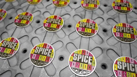 PA Media Multiple of the coloured coin laid out on a surface. it features all five members: Victoria Beckham, Melanie Chisholm, Emma Bunton, Geri Halliwell-Horner and Melanie Brown - captured in a silhouette alongside their autographs.