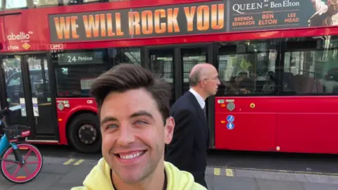 Jarryd Nurden Jarryd Nurden in a yellow top posing in front of a London bus with a We Will Rock You