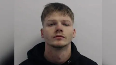 A police mug shot of James Lamb, who wears a black hoodie and looks into the camera without smiling