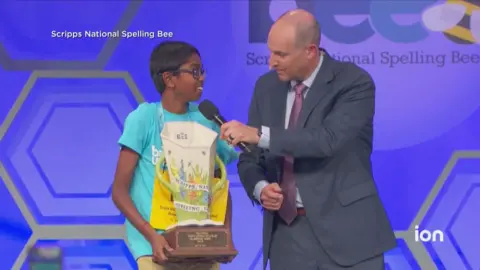 Bruhat Soma holding trophy beside spelling bee host