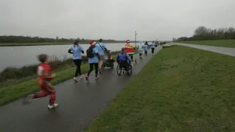 BBC Image of people running, walking, pushing and wheeling by Dorney Lake in Windsor.